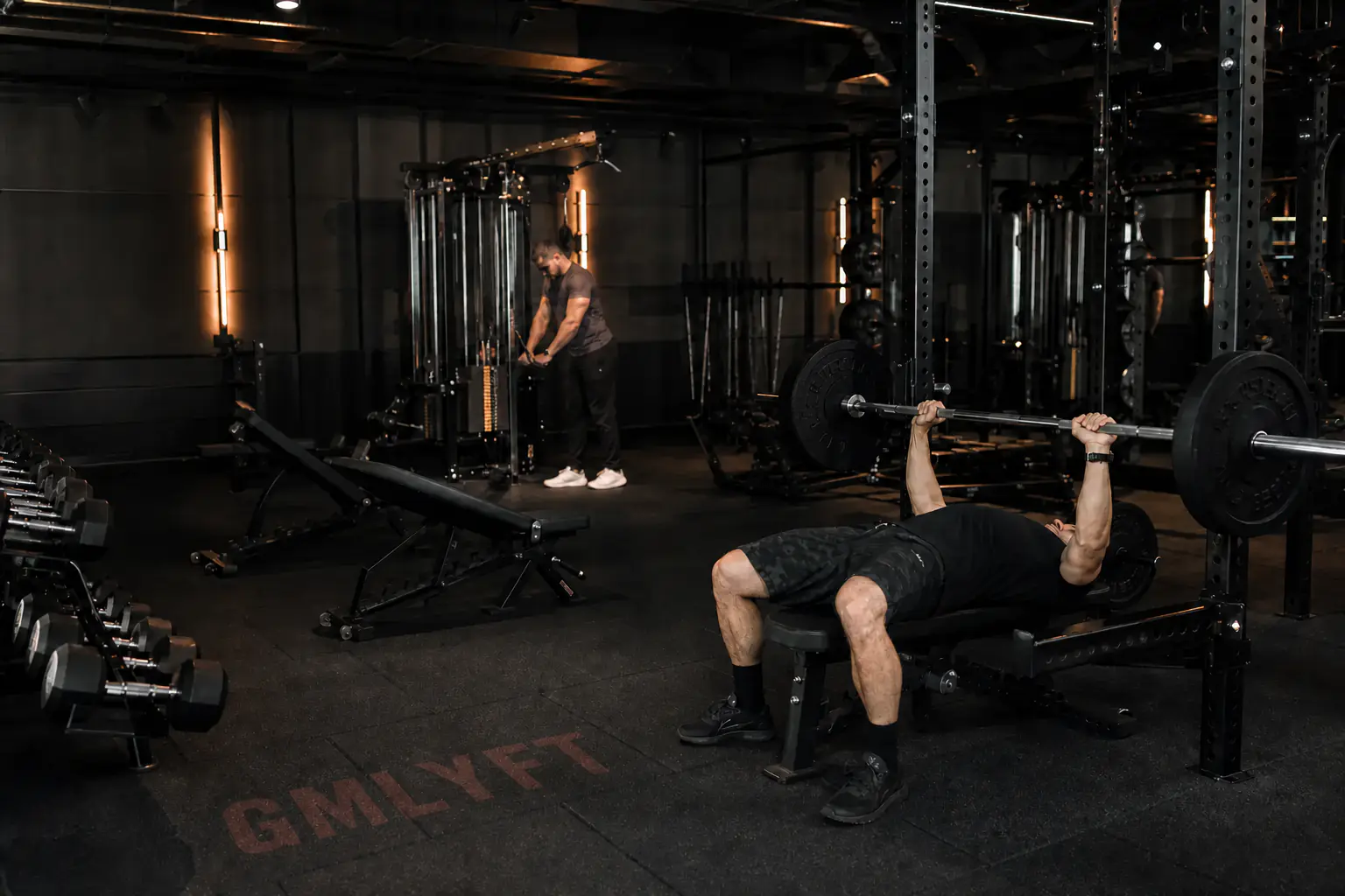 Lifter using a bench press with dumbbells and cable equipment nearby